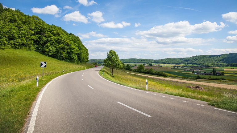 Country road surrounded by greenery with a blue sky.