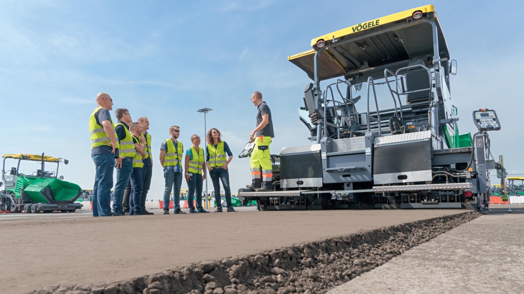 Training group with safety vests in front of Vögele paver