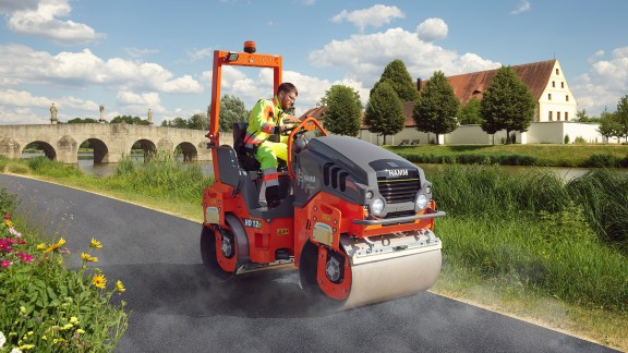 A battery-powered Hamm electric tandem roller compacting a stretch of road.
