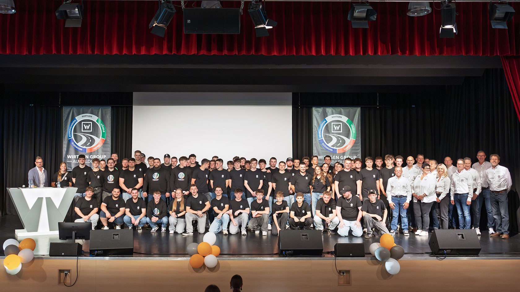 Gruppenfoto der aktuellen Auszubildenden und ihrer Ausbilder auf der Bühne bei der Jubiläumsfeier