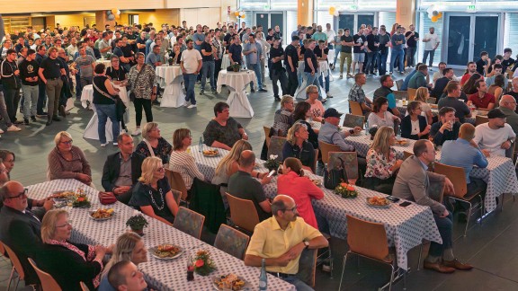 Menschen sitzen und stehen in einem hellen Veranstaltungssaal.