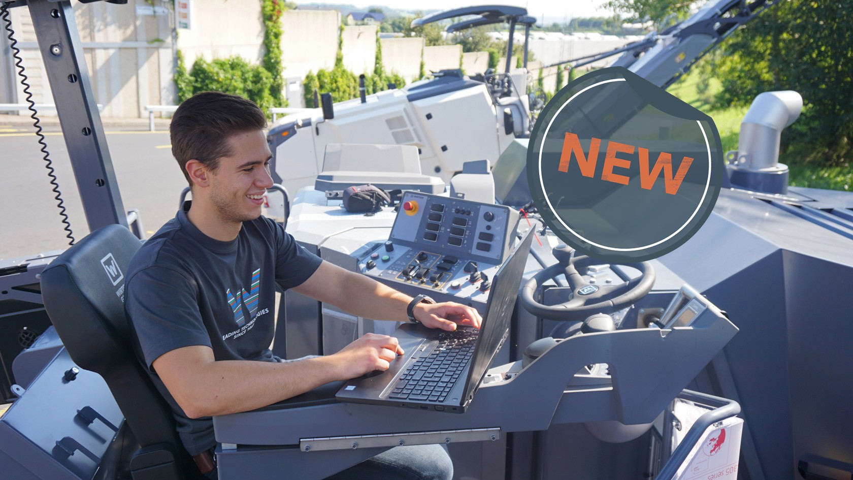 Smiling young student with laptop sitting at the control panel of a cold milling machine