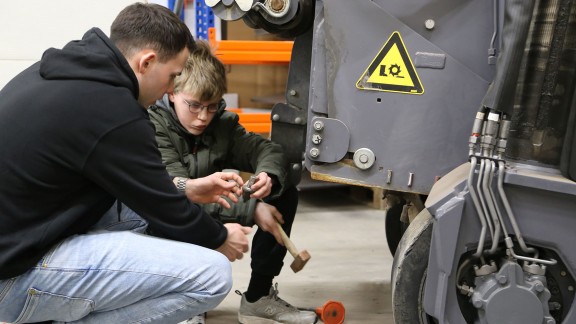Ein Mann und ein Junge schlagen einen Meißel mit einem Hammer in eine Fräswalze