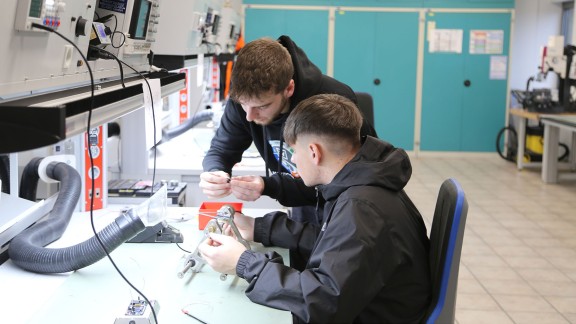 Männlicher Azubi erklärt Jungen ein Elektroteil