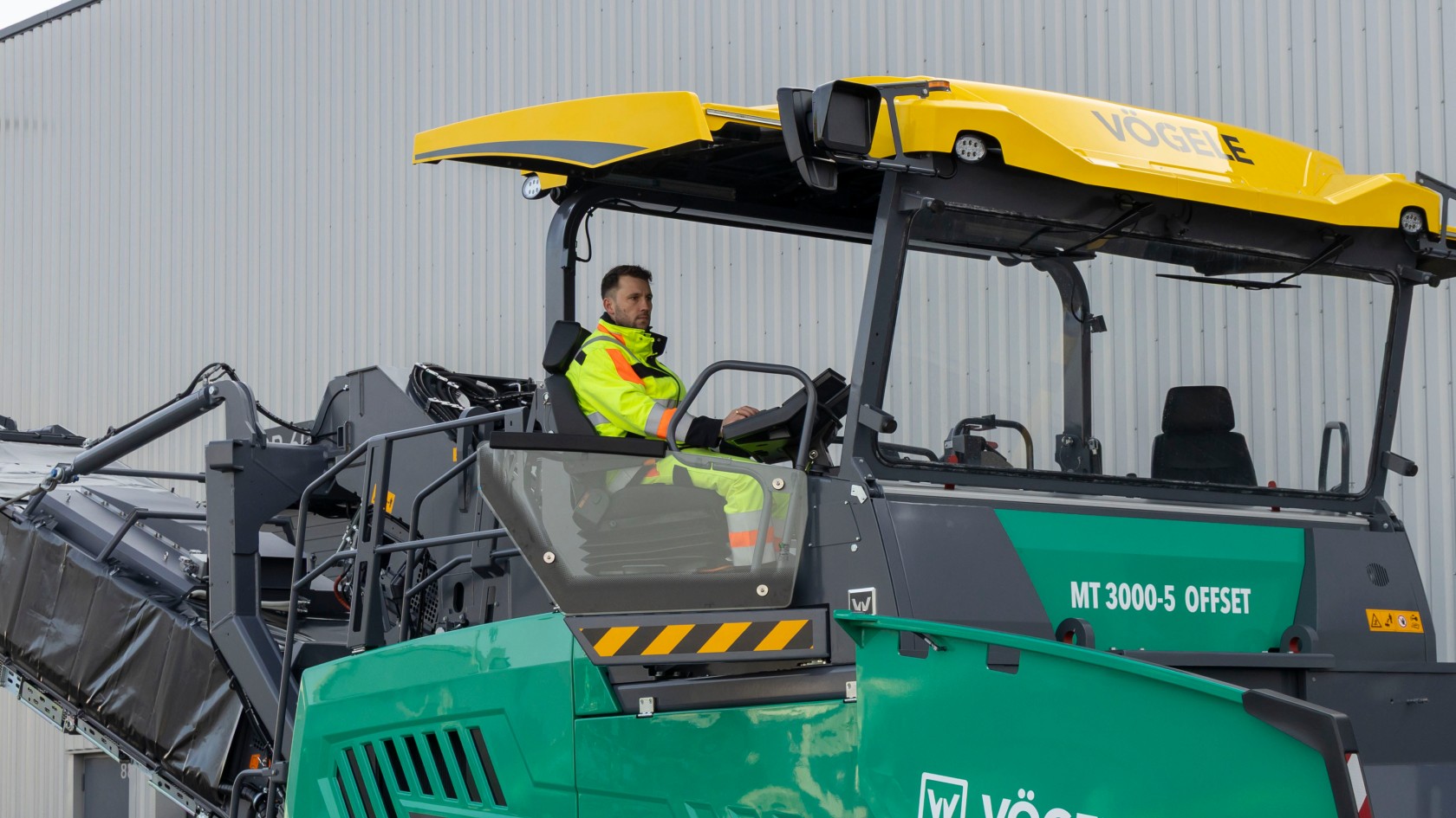 The photo shows the seated operator on the ErgoPlus 5 operator’s platform of a VÖGELE MT 3000-5 Offset PowerFeeder.