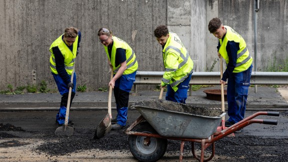 Trainees shoveling excess asphalt into a wheelbarrow.