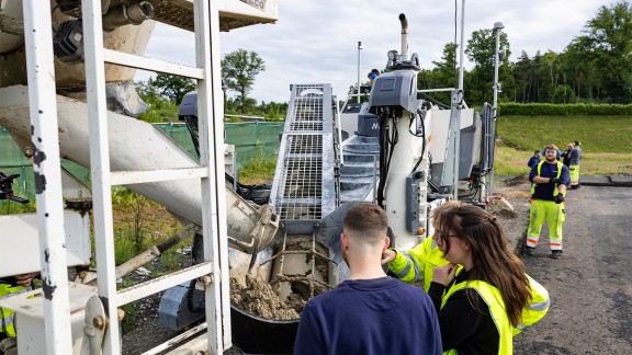 The trainees alongside the Wirtgen slipform paver take a closer look at the belt conveyor and the concrete feeding system.