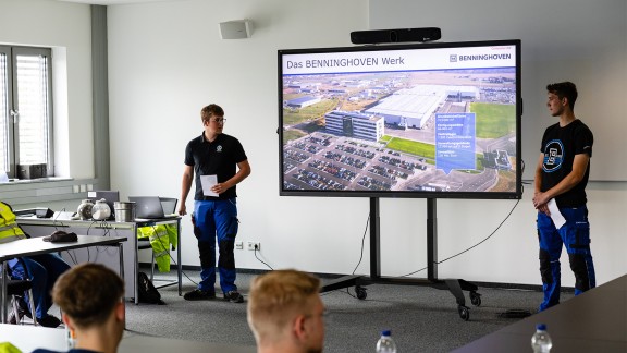 Two young men making a presentation. The presentation is displayed on a large monitor screen between them.