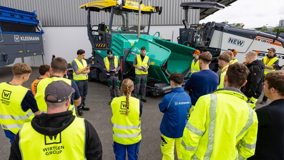 Trainees looking at a Vögele paver with three young men in front of it giving a talk.