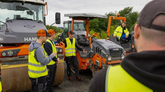 Trainees standing in front of three Hamm rollers and listening to an instructor.