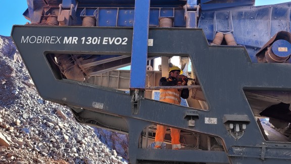 Вид дробилки сбоку: Оператор выполняет замену сита для предварительного грохочения снизу; верхняя дека не демонтируется.