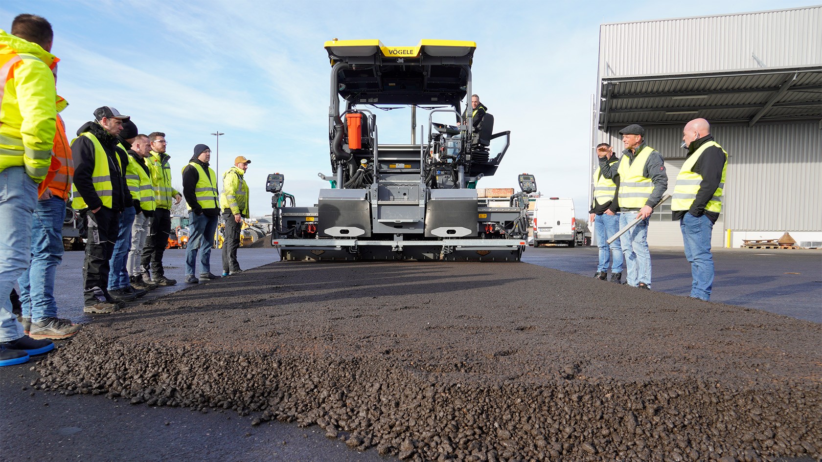 Group of machine operators watching asphalt paving with a Vögele paver.