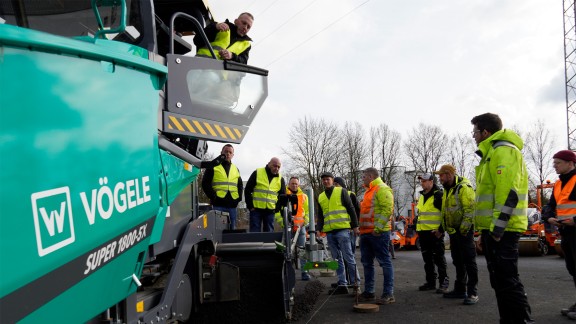Outdoor scene of a group looking at a paving screed and listening to their instructor.