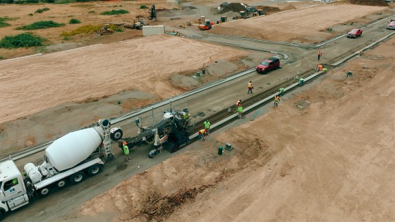 Surface libre, on y voit la future route, au premier plan la SP 15i et un camion malaxeur lors de la pose des bordures de béton et des rigoles.