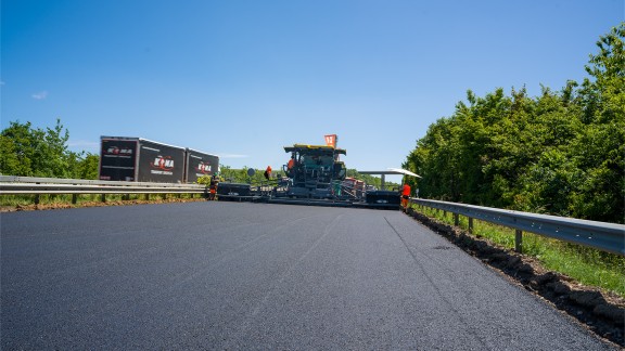 The paved surface layer - in the background, the paver with its screed covering the full width of the highway.