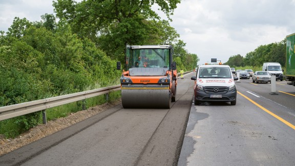 A tandem roller compacts the first road layer.