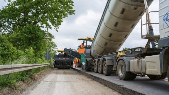 The cold mix is loaded onto the mobile feeder. The mobile feeder passes the mix on to the paver.