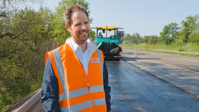 Man wearing hi-vis vest standing in front of a Vögele paver on the autobahn