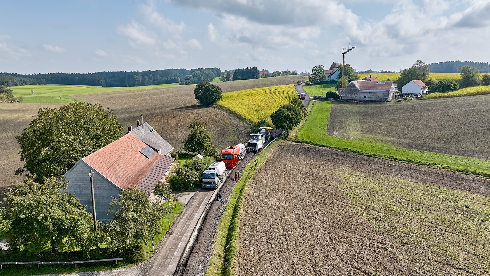 Bird’s eye view of the cold recycling train in idyllic countryside with a house.