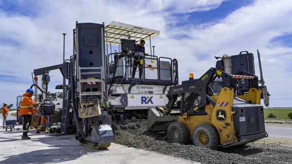 John Deere Grader evenly spreads the concrete ahead of the slipform paver.