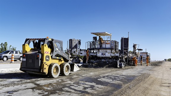 John Deere Grader evenly spreads the concrete ahead of the slipform paver.