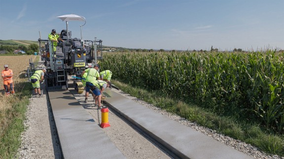 Paving a two-track road profile in Sieghartskirchen, with the SP 33 in the background and workers in the foreground