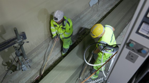 View from above of two workers next to the paved kerb-gutter profile in the Semmering Tunnel.