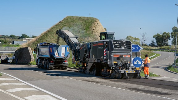 The W 210 XF offloads the milled material to a transport vehicle in front of a heap of material.