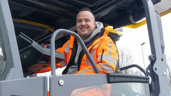 Paver operator smiling into the camera from the paver operator’s cab.