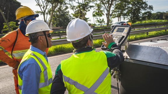 Service staff explaining the paver operator’s console to two workers.