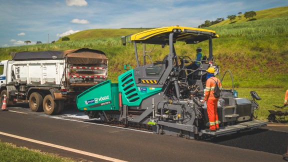 Oblique view from the rear of the SUPER 2100-5 X paver with a truck in front of it.