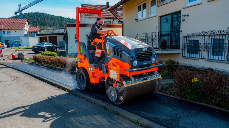 HD 12e VT compacting the asphalt layer on a footpath with houses in the background.