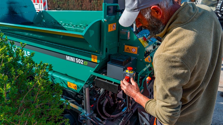 Material hopper of the MINI 502e, with worker checking the transfer of the asphalt mix.