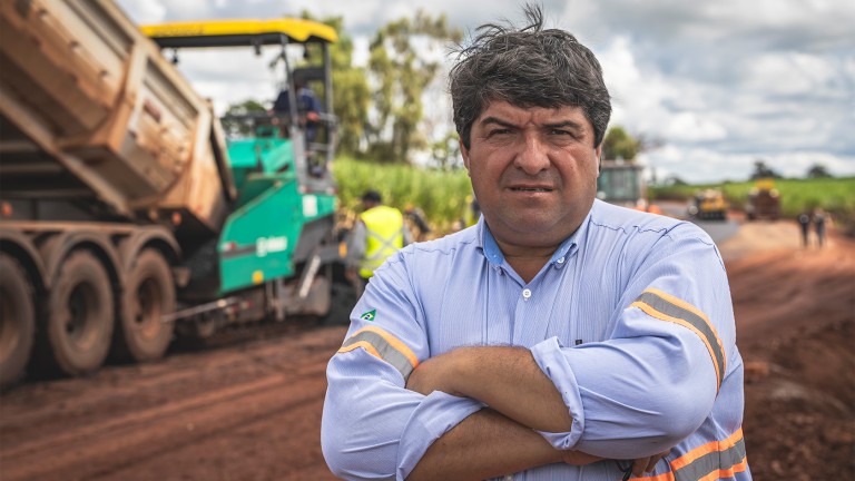 Retrato de Carlos Adriano, Diretor de Produção da Usina Alta Mogiana, com a pavimentadora Vögele ao fundo.