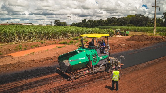 Pavimentadora Vögele SUPER 1400 em operação, cercada por canaviais.