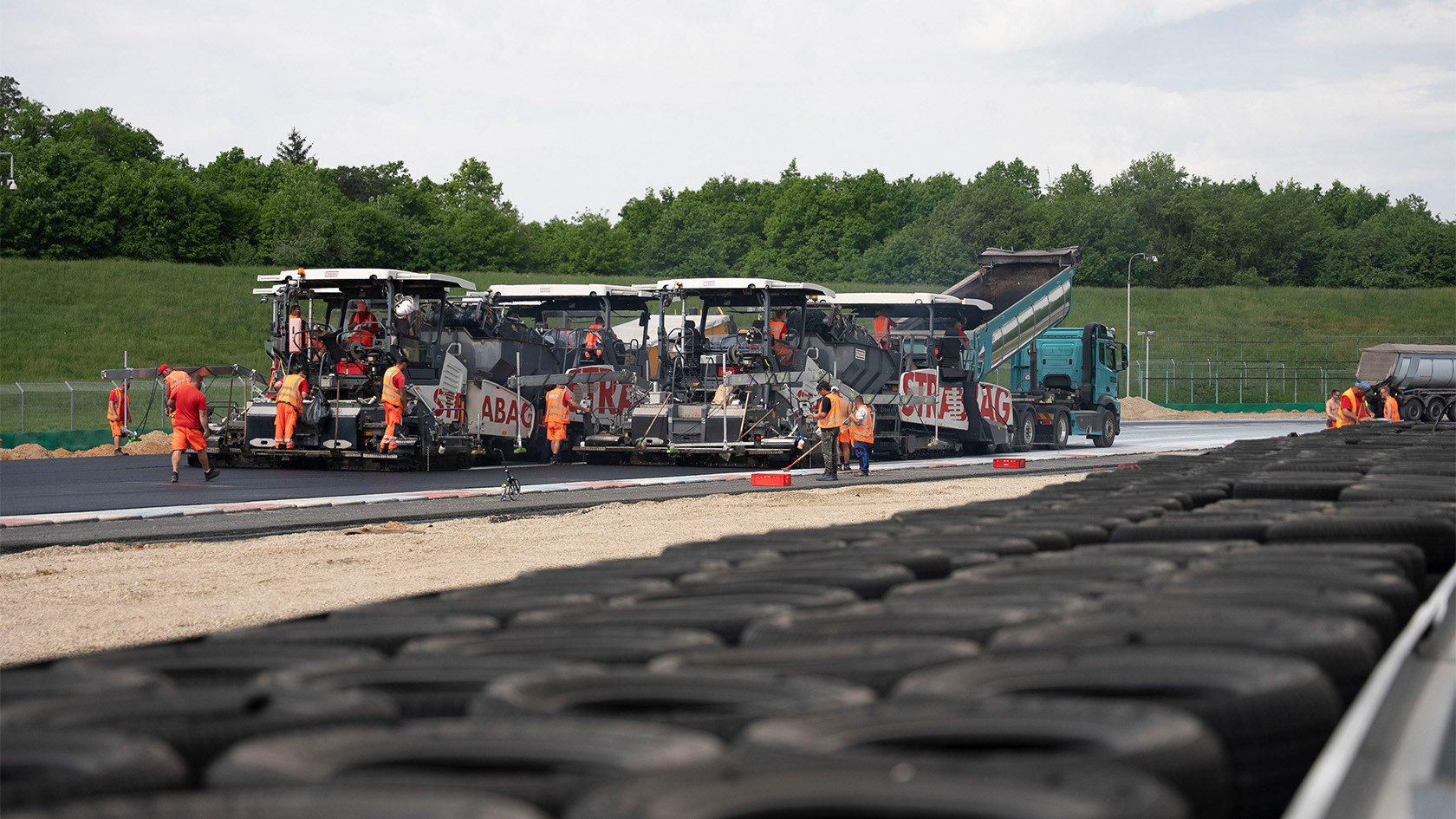 Vögele Pavers paving asphalt on a race track with car tyres in the foreground.