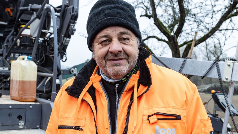 A middle-aged gentleman wearing brightly coloured weatherproof clothing and a cap on his head looks into the camera with a friendly smile.