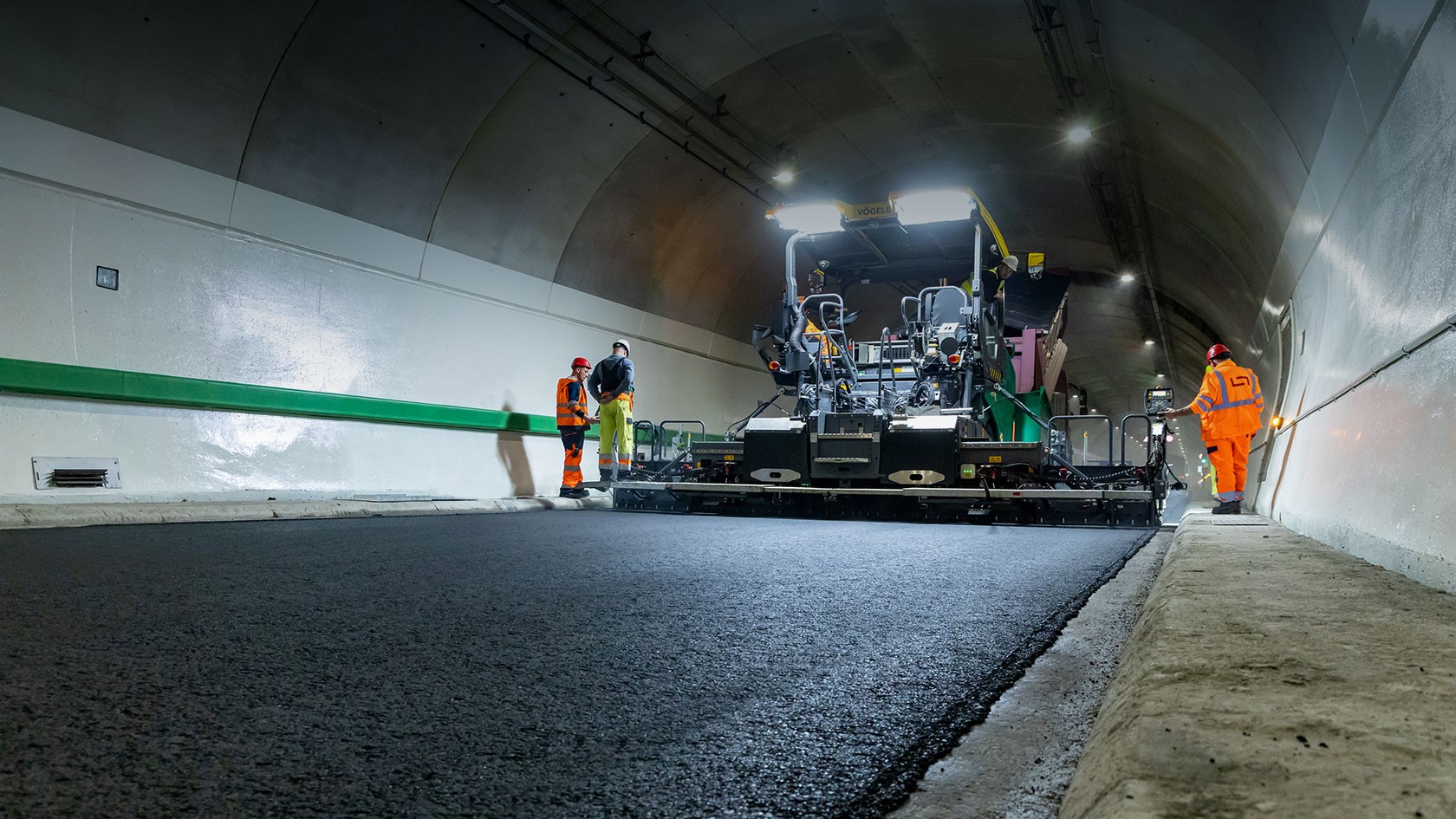 Working in the tunnel: the foreground shows the paved surface course, whilst in the background, several workers can be seen standing next to the Vögele SUPER 1803-5 X wheeled paver.