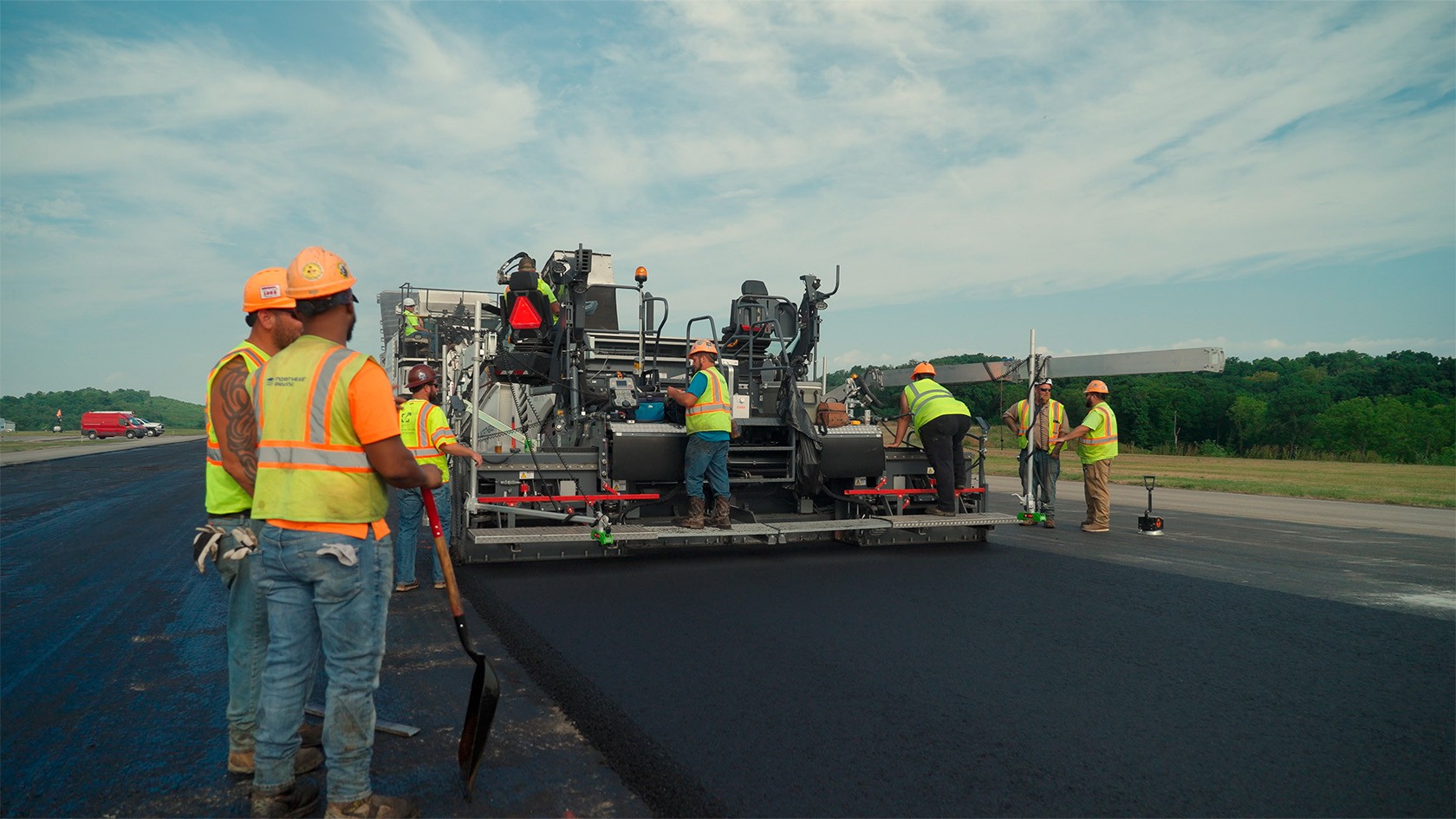 Le SUPER 2000-3i lors de la réfection de la piste, au premier plan sur le côté, deux travailleurs qui observent le processus de pose.