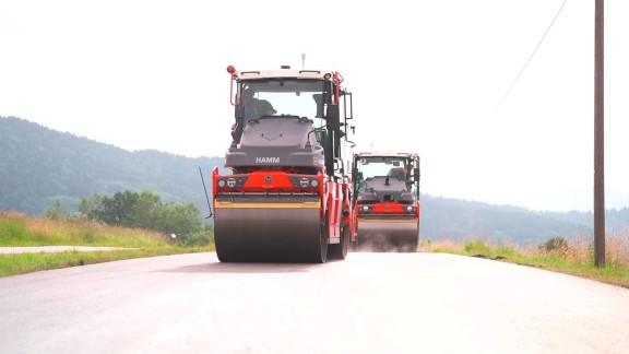 Two rollers driving up a hill in the sunshine.