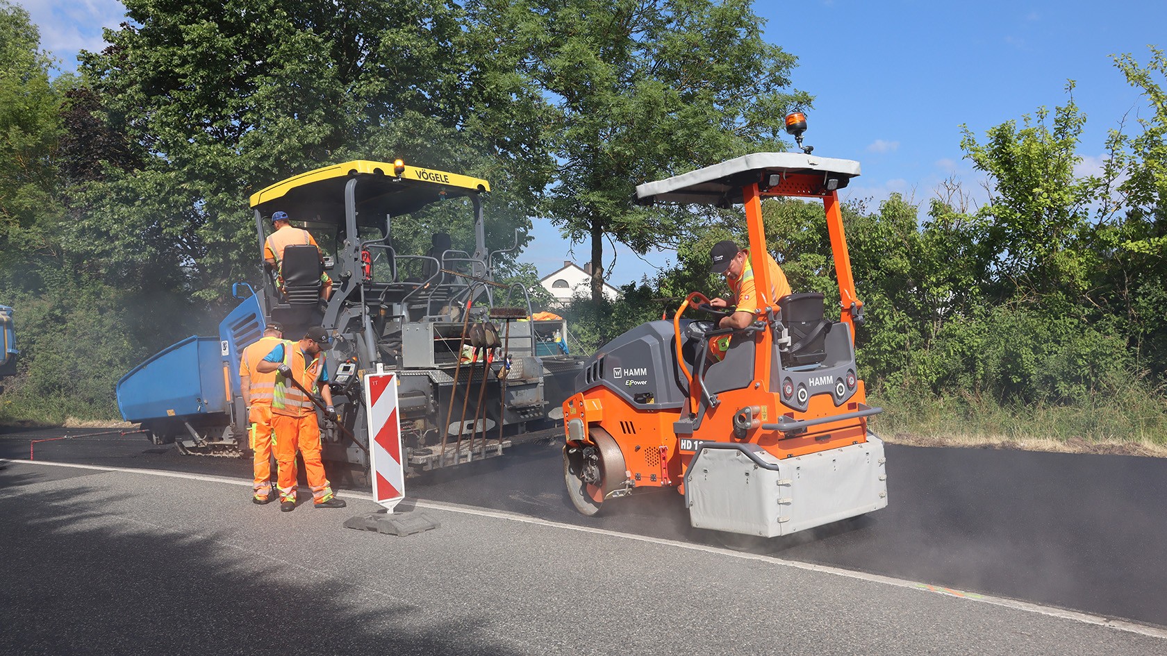 A tandem roller compacts a newly paved asphalt layer behind a street paver.