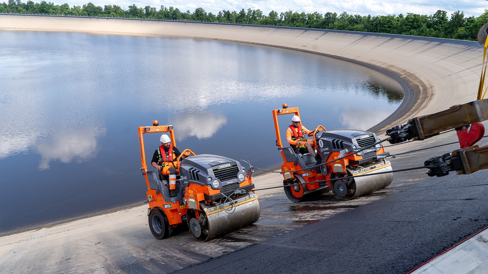 Two tandem rollers compacting freshly laid asphalt on an incline.