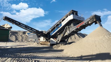 A low, oblique view of a classifying screen with a large heap of stone in front of the plant.