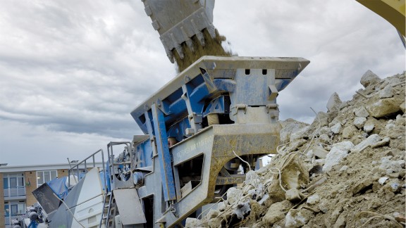 Close-up of the feed hopper; in front of it a pile of mixed rubble with metal rods.