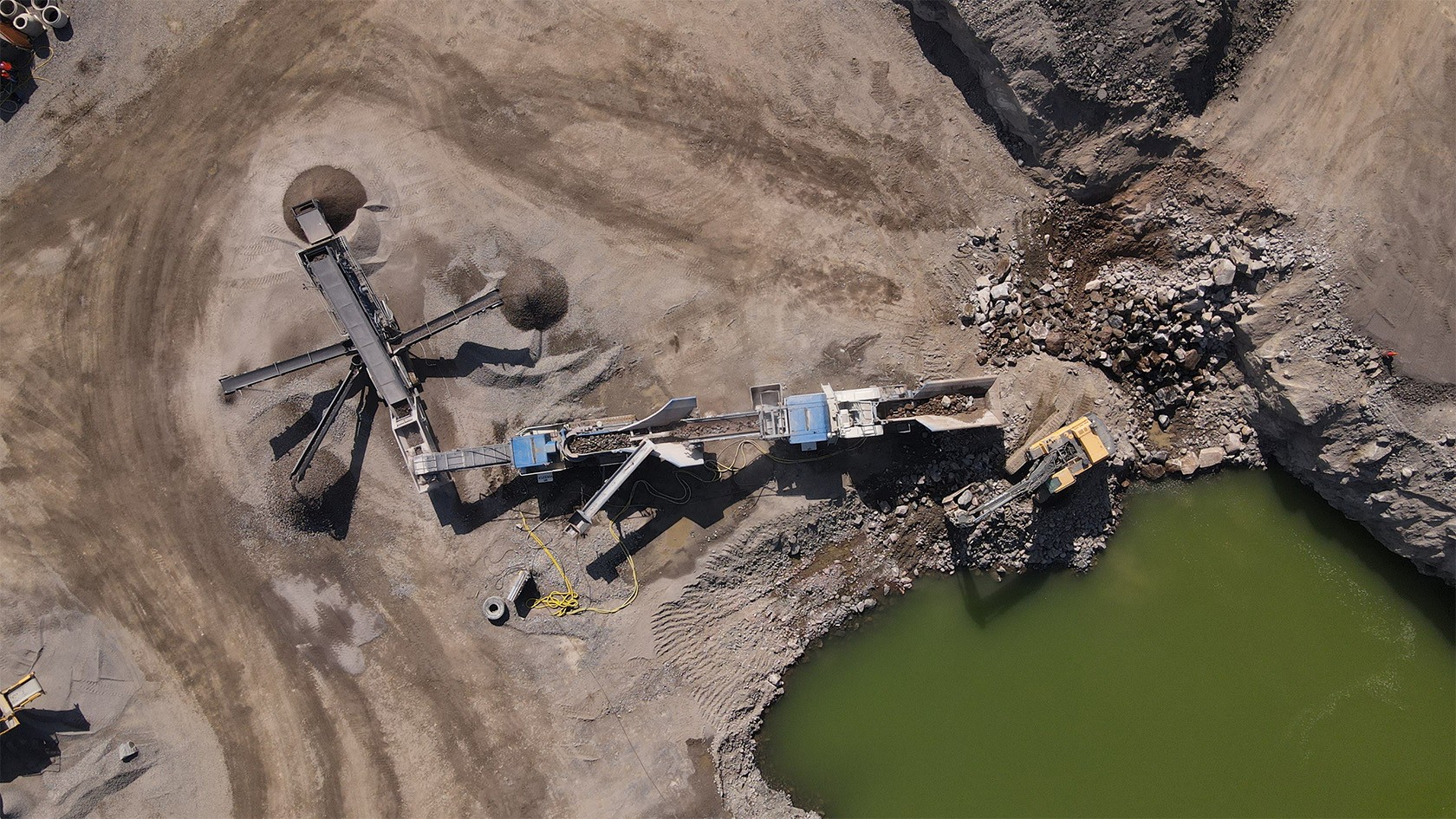 A bird’s eye view of the plant train in a quarry. In the foreground, a bright green quarry lake.
