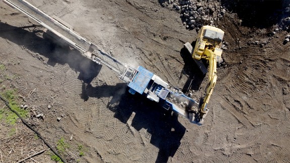 Aerial view of the MC 110i EVO2 with an excavator tipping volcanic rock into the feed hopper, view of the belt conveyor from above