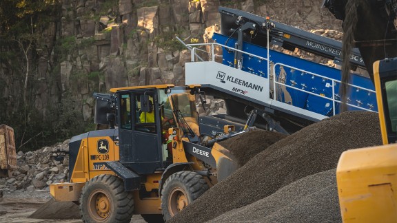 A John Deere front loader working in the quarry in front of the Kleemann classifying screen.