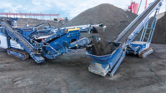 La trituradora de impacto y la criba llenan el depósito de material de la cinta de vaciadero.