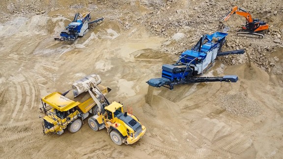 La MR 130 PRO produce en un solo paso de trabajo tres granulometrías. Al mismo tiempo, una pala cargadora sobre ruedas John Deere carga el producto final en un camión. Vista aérea.