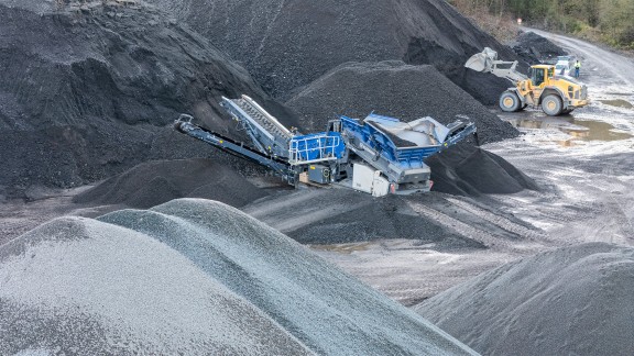 L’impianto di vagliatura mobile si trova tra montagne di vecchio asfalto rotto e seleziona varie granulometrie.